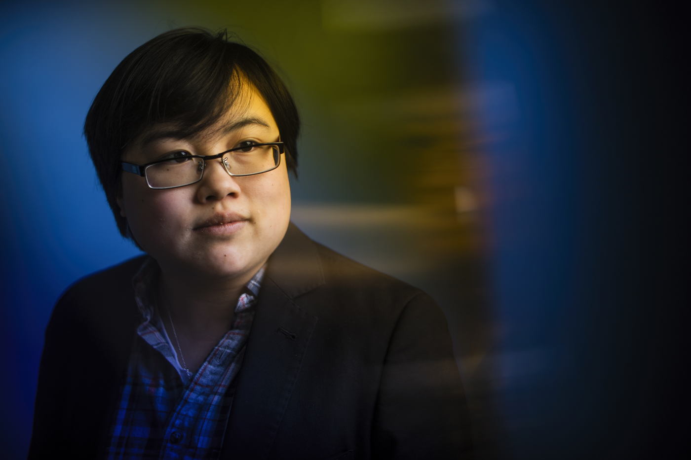 [Photo: Headshot of Lydia Brown, young East Asian person, with stylized blue and yellow dramatic background. They are looking in the distance and wearing a plaid shirt and black jacket. Photo by Adam Glanzman.]